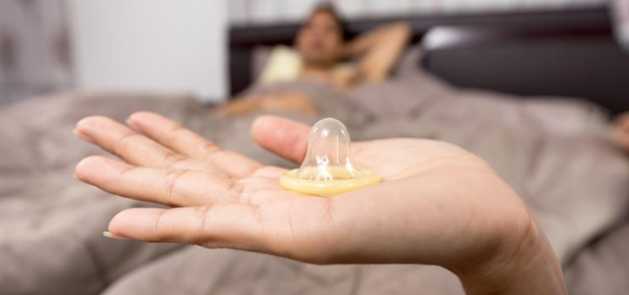 Frau hlt im Bett Kondom in der Hand als Verhtungsmethode nach der Geburt
