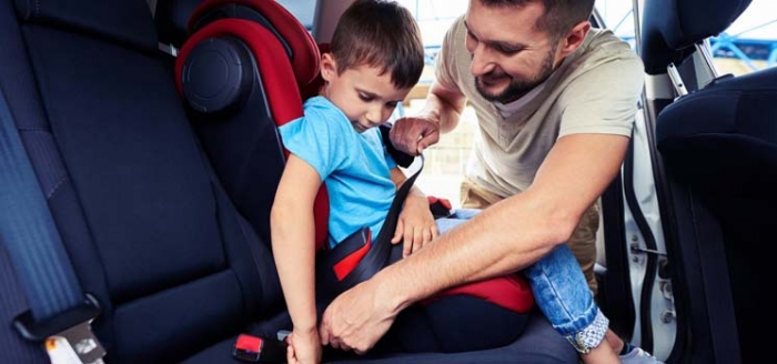 Vater schnallt Sohn im Autokindersitz an, denn sie verbringen viel Zeit im Auto als Teil des Landlebens