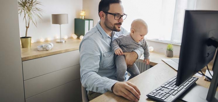 Vater arbeitet mit Baby auf dem Arm zuhause in Elternzeit Vater arbeitet mit Baby auf dem Arm zuhause in Elternzeit