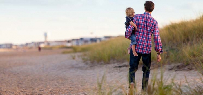 Vater hat sich den Kinderwunsch beim Mann erfllt und hlt sein Kind am Strand auf dem Arm