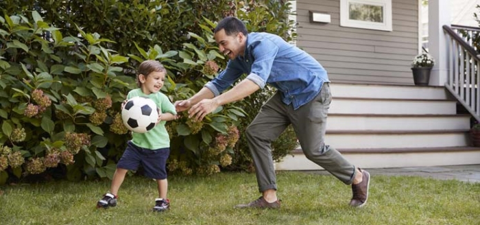 Vater spielt mit Sohn Fußball im bezahlbaren Wohnraum auf dem Land