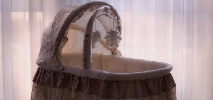 Babywiege vor weißer Gardine, die Lichtschutz für Kinder spendet Babywiege vor weißer Gardine, die Lichtschutz für Kinder spendet