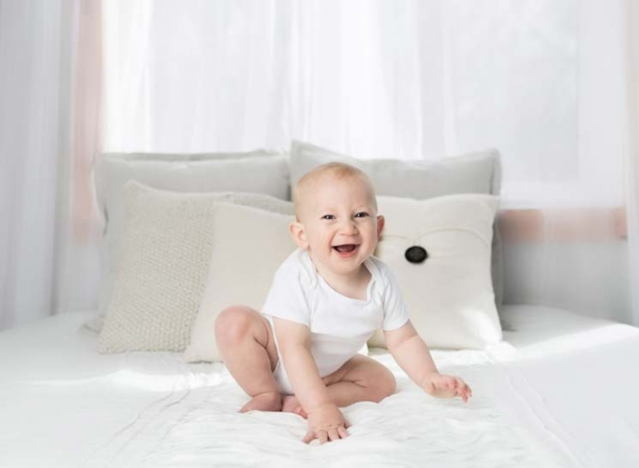 Baby lacht auf Bett vor teilweise abdunkelnder Gardine